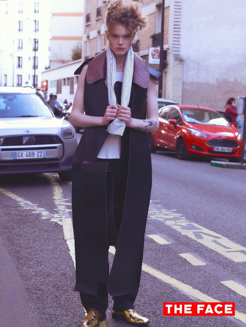 Model wearing a dark long vest and striped scarf standing on an urban street between parked cars for The Face China editorial.