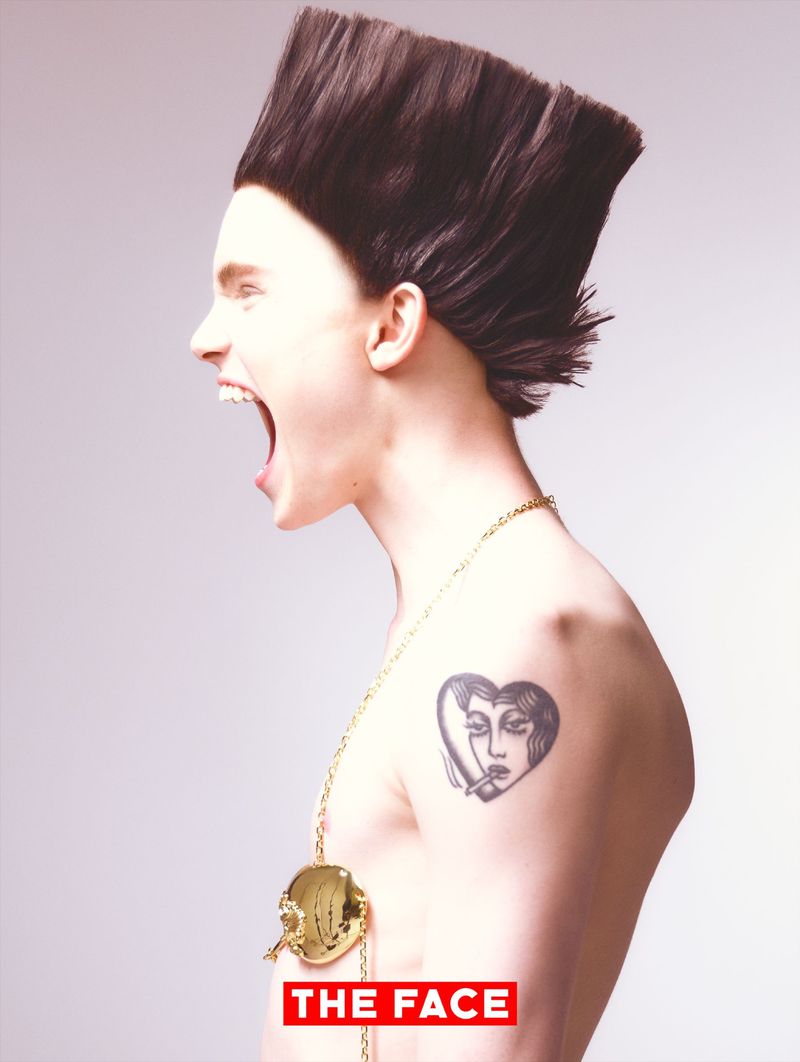 Model Malte Carlsson shouting in profile with an exaggerated square flat-top hairstyle and heart tattoo against a white studio backdrop.
