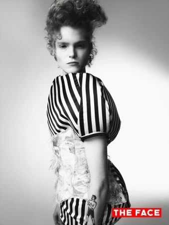 Model Malte Carlsson posing in a black and white striped garment with a corset overlay against a studio backdrop.