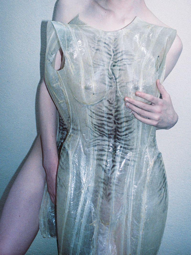 Model Victoria Volt posing in a translucent sculptural dress with tiger stripe markings against a neutral wall.