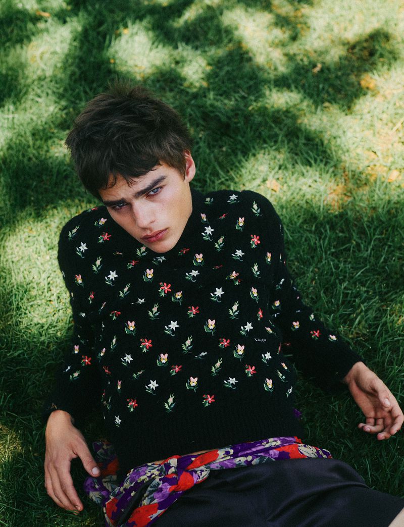 Model Jon Payeras reclining on grass in a black floral embroidered sweater for Numéro Istanbul.