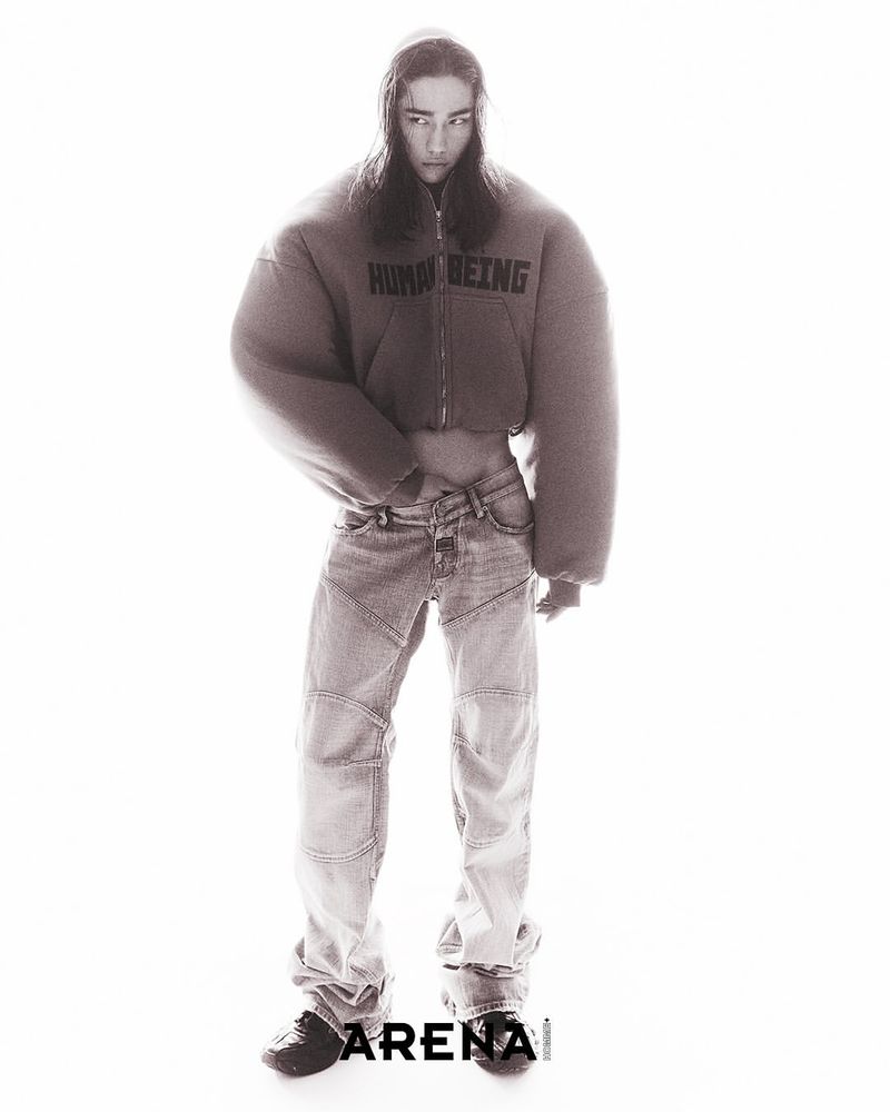 Model Ilias Dosumbaev posing in an oversized cropped brown zip-up hoodie and baggy denim jeans against a bright white background.