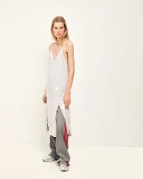 Model wearing a pale embellished slip dress over wide-leg grey track pants with red stripes against a plain studio background.