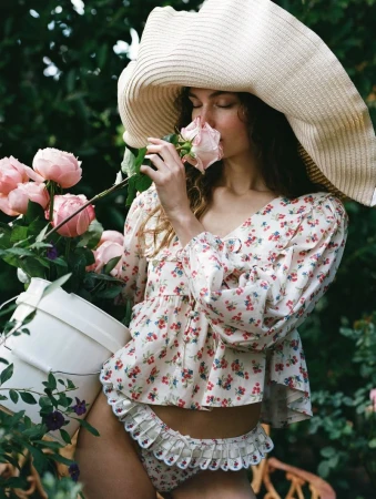 Model wearing a large straw hat smelling a pink rose while holding a bucket of flowers