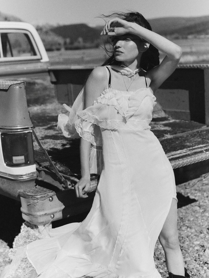 Model Valerie Pasker wearing a ruffled white lace wedding dress while leaning against the open bed of a vintage pickup truck.