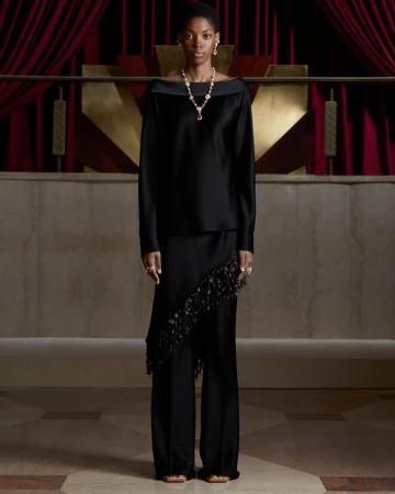 Model in a black off-the-shoulder satin ensemble wearing a Dior high jewelry gemstone necklace against red velvet curtains.