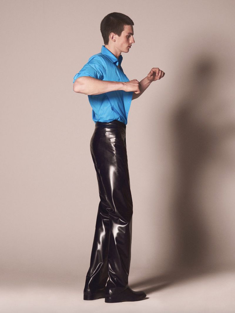 Model wearing a vibrant blue shirt and glossy black trousers against a neutral studio background.
