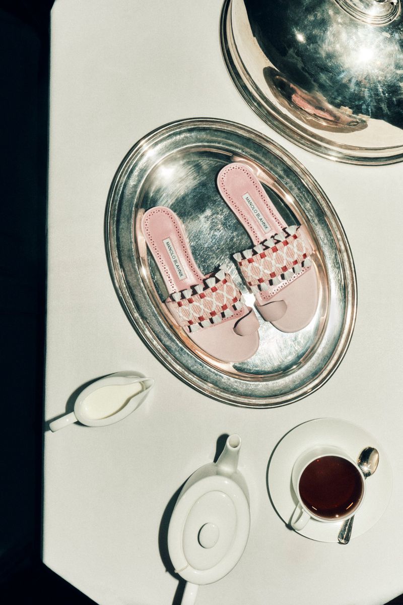 Pair of pink patterned flat sandals on a silver serving platter beside a white teapot, tea cup, and creamer pitcher on a white surface.