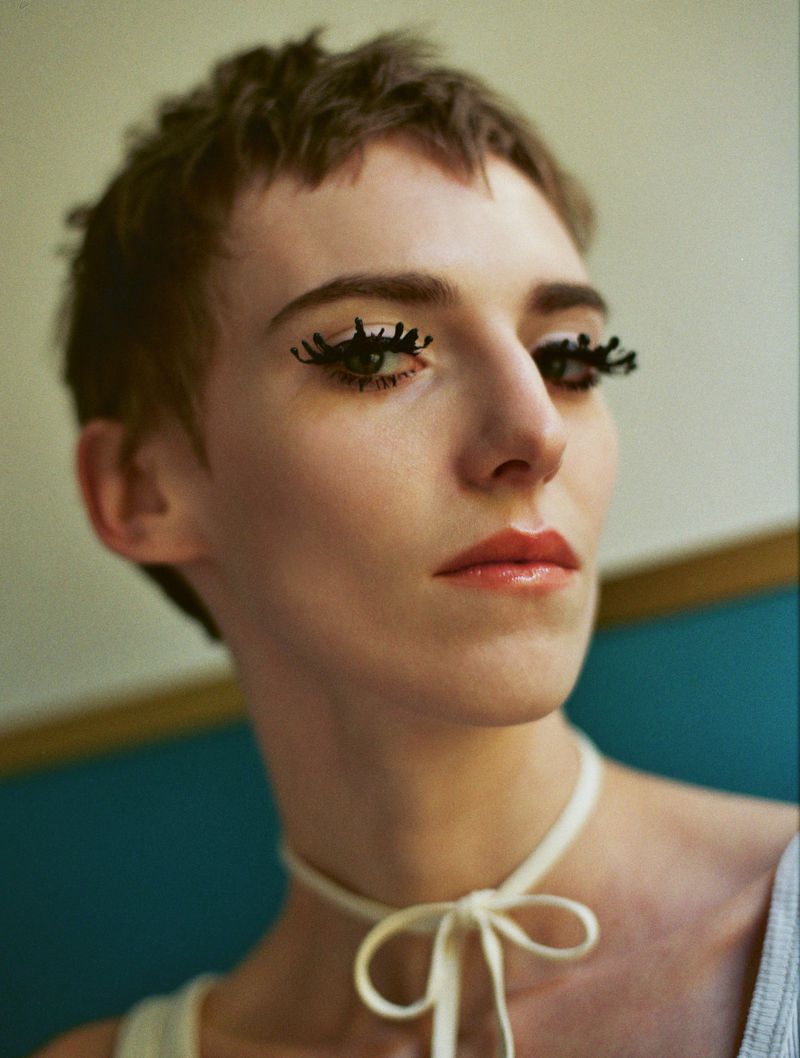 Close-up portrait of a woman with striking eye makeup and a ribbon choker, set against a simple background, emphasizing beauty and style.