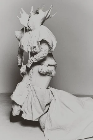 Monochrome fashion portrait of a model wearing an avant-garde white corset gown with a jagged sculptural collar in a studio.