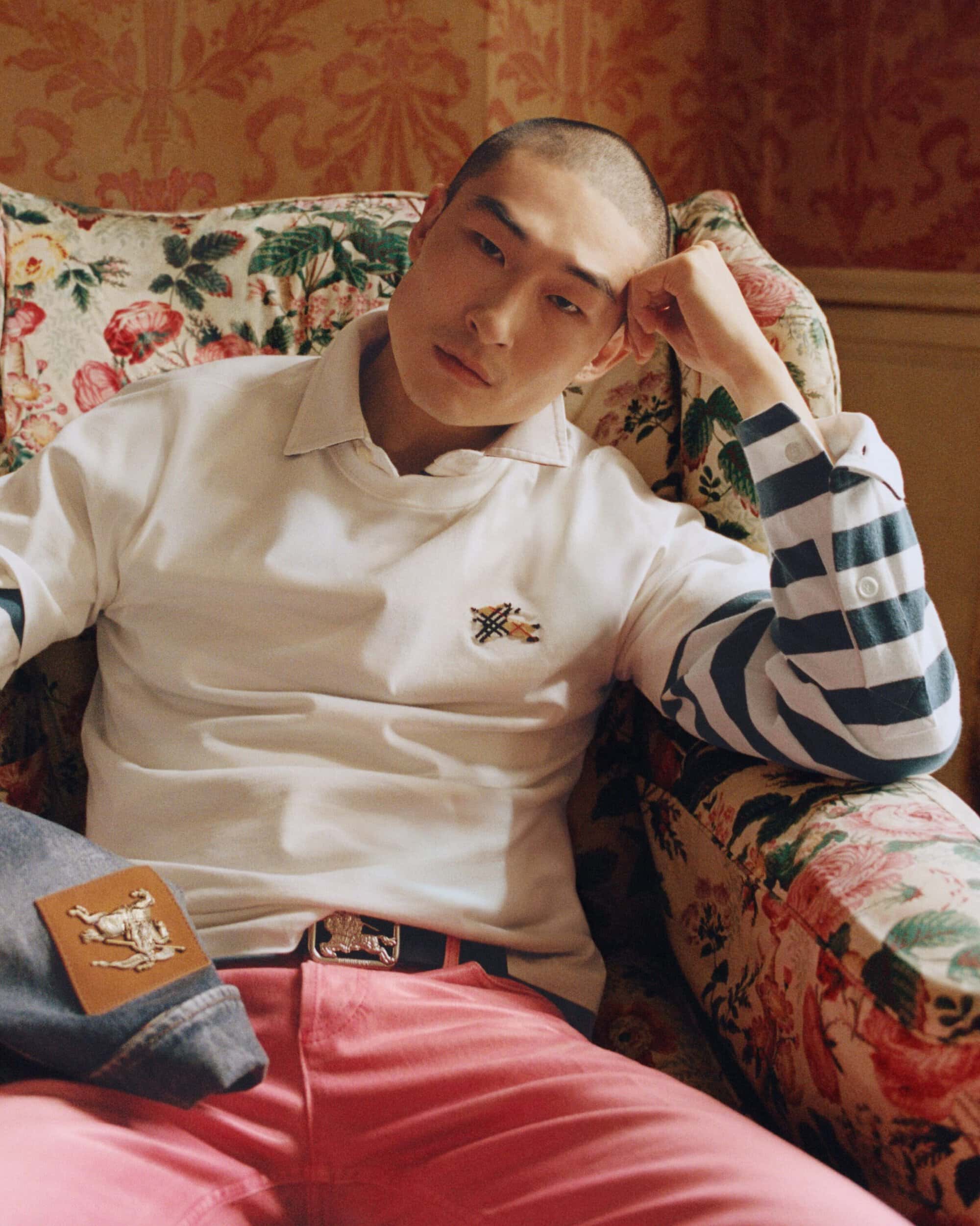 Sang Woo Kim seated in a floral armchair wearing a white collared shirt and pink trousers for Burberry