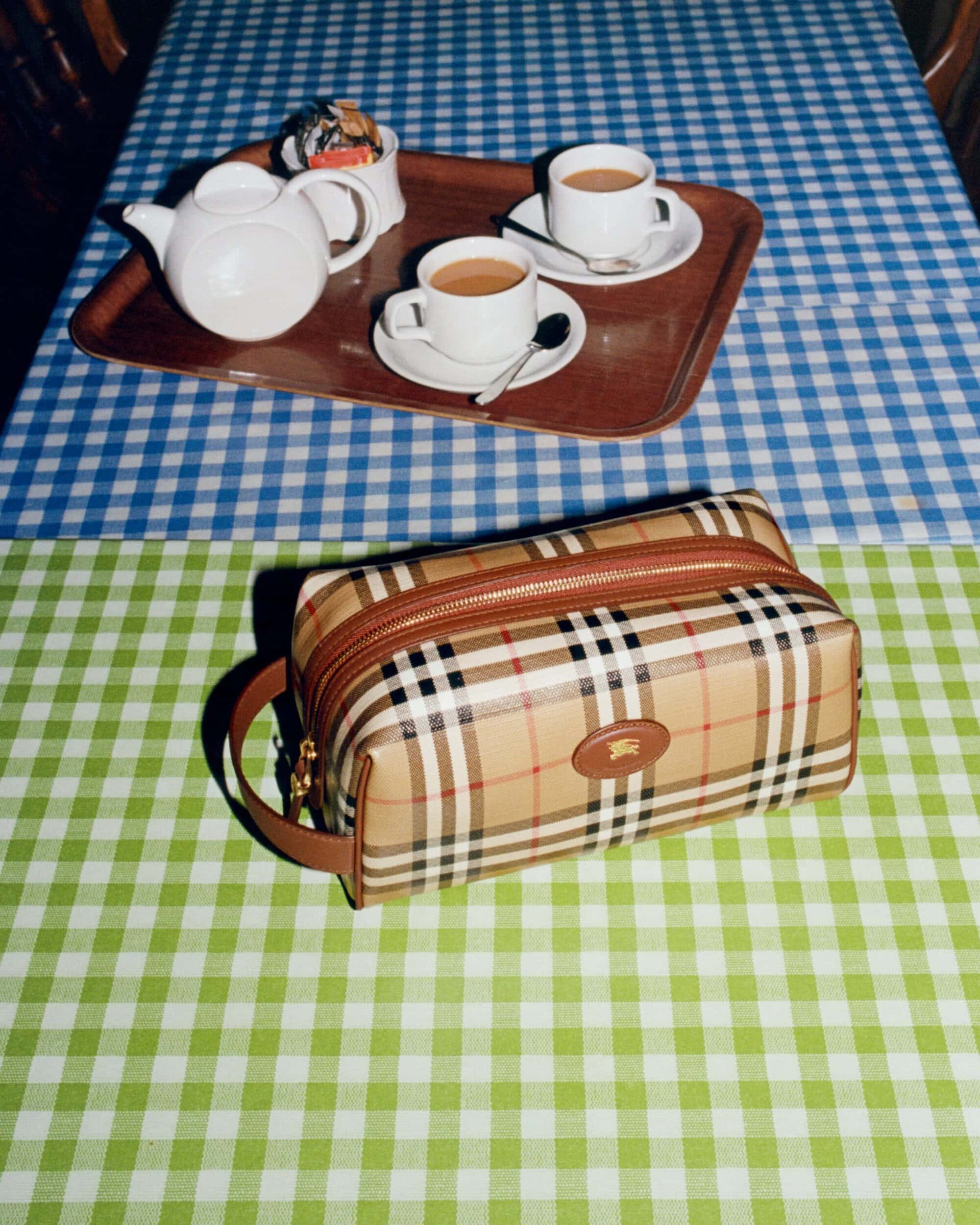 Burberry vintage check toiletry bag on a green and blue gingham tablecloth beside a tea set on a serving tray.