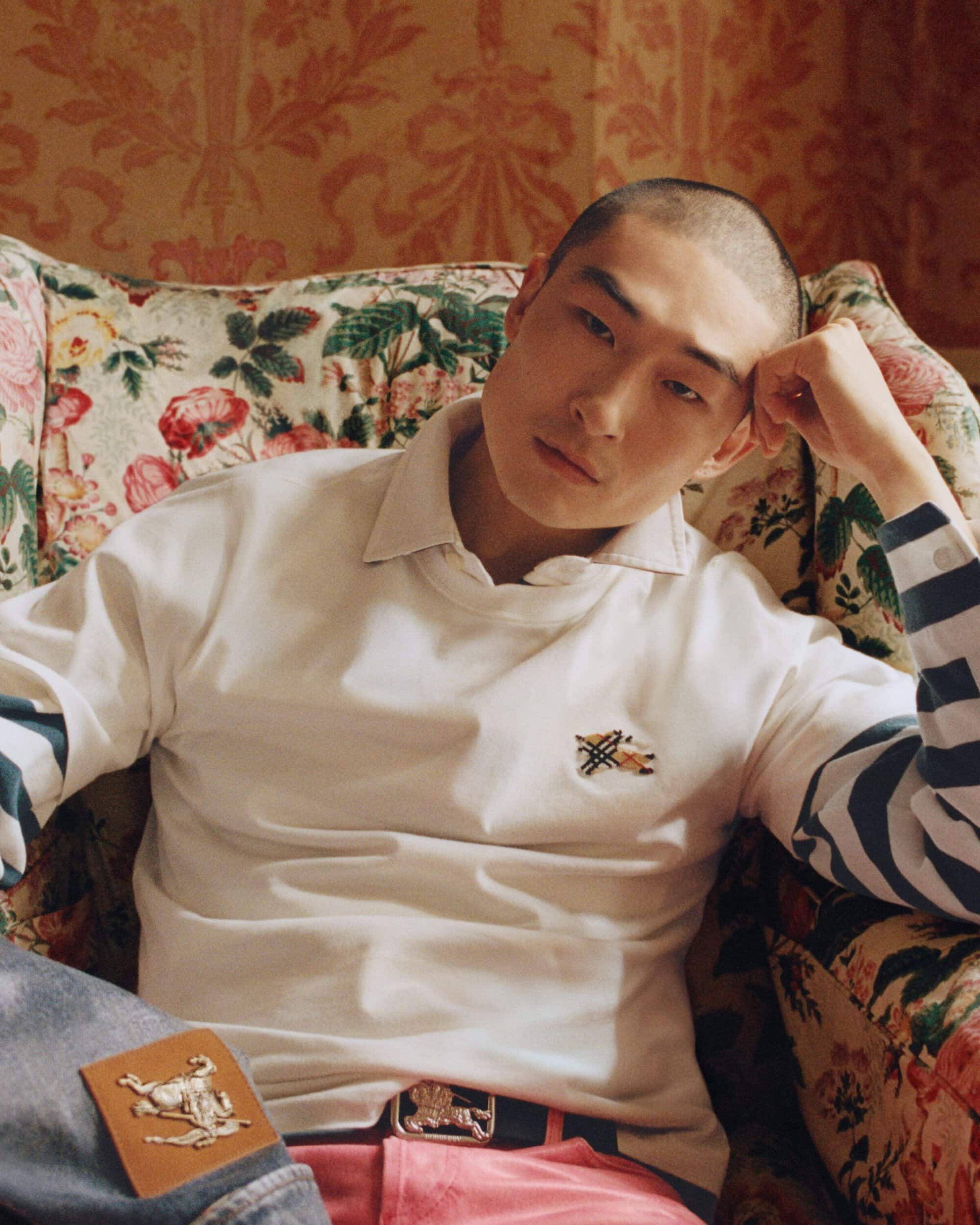 Sang Woo Kim seated in a floral armchair wearing a white collared shirt for Burberry