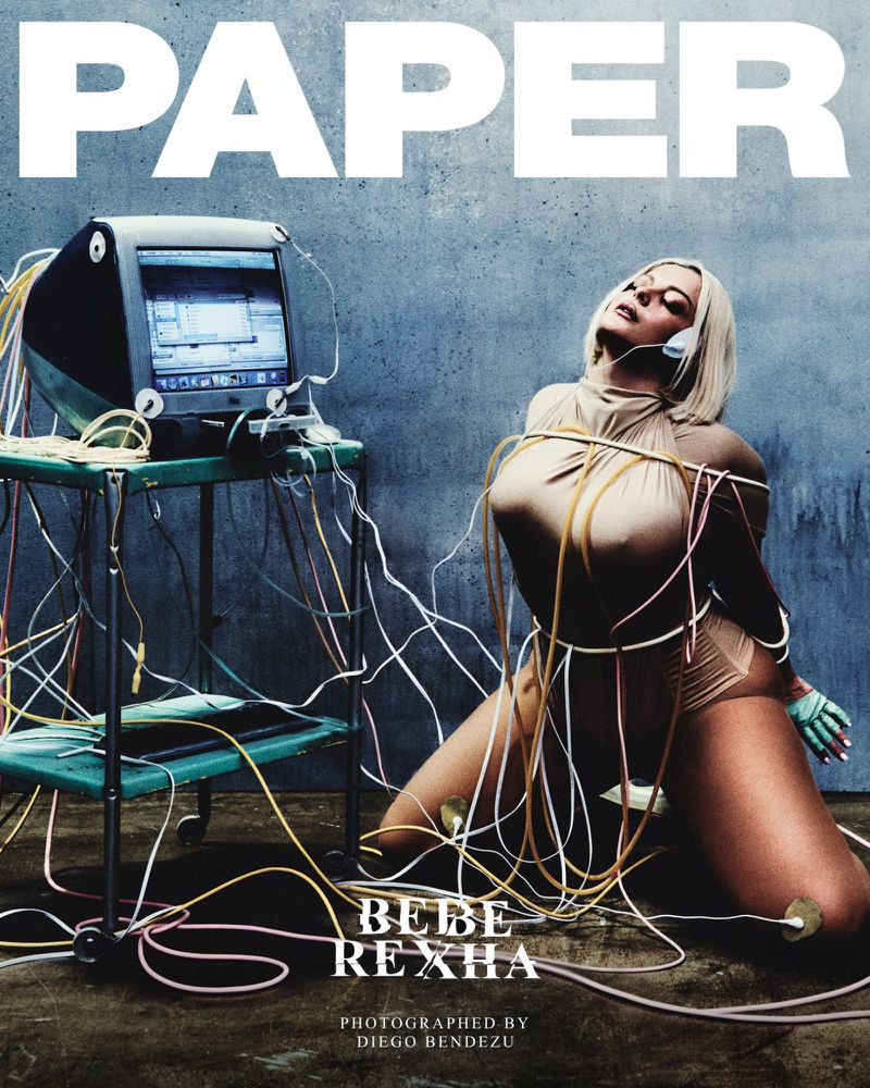 Bebe Rexha kneeling in a beige bodysuit bound in computer cables beside a vintage monitor for Paper Magazine.