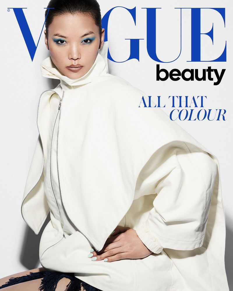 Model Xue Huizi in an oversized off-white structured high-collar coat with vivid blue eye makeup for a Vogue cover against a white backdrop.