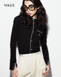 Model Xue Huizi wearing oversized round sunglasses, a black piped button-down shirt, and cream trousers against a white studio background.