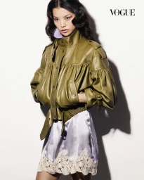 Model Xue Huizi posing in an olive green gathered leather jacket and lilac lace-trimmed satin dress against a white background.