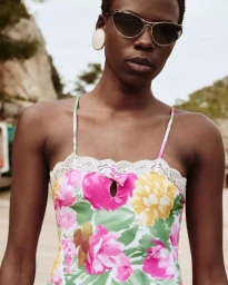 Model Agel Akol wearing sunglasses, a large white button earring, and a floral lace-trimmed camisole top.
