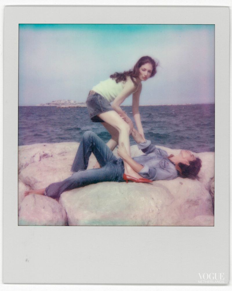 Polaroid photograph of a female model standing over a male model lying on rocky coast by the ocean
