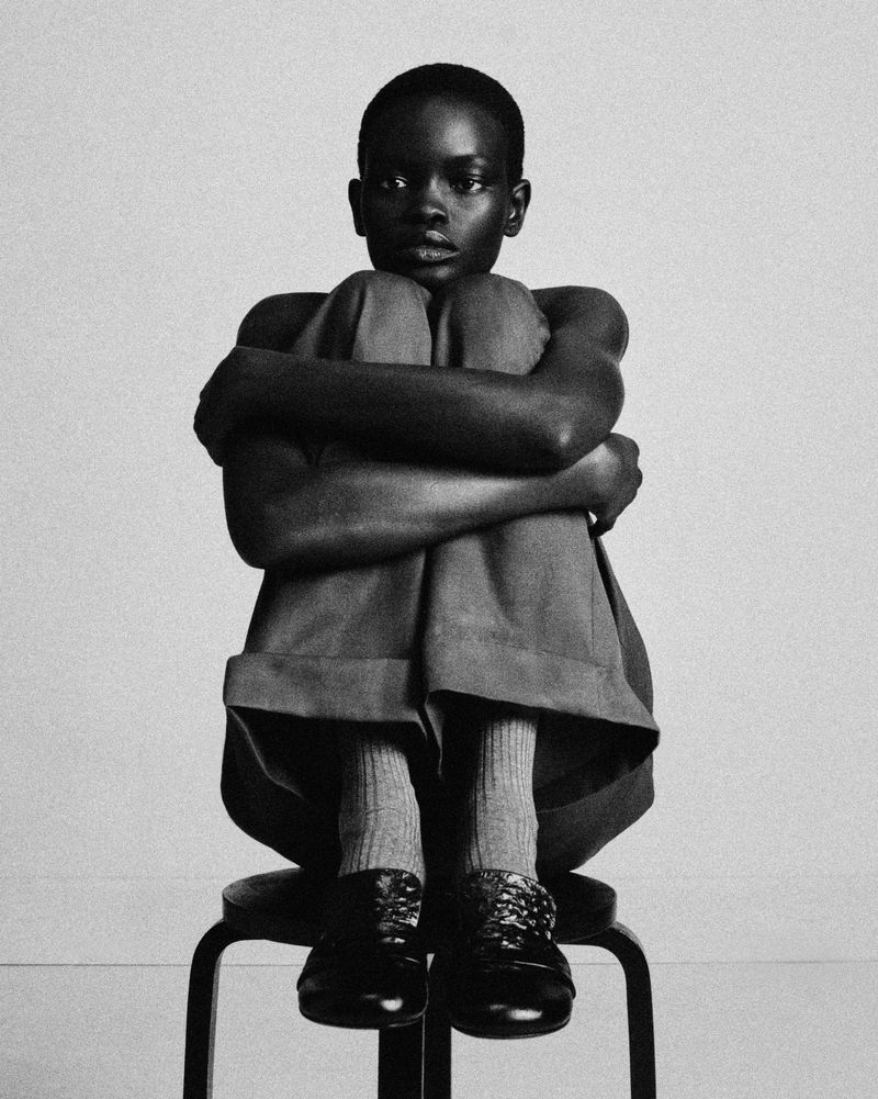Monochrome portrait of model Athiec Geng seated on a dark stool with arms wrapped around knees for Acne Paper Autoportrait II.