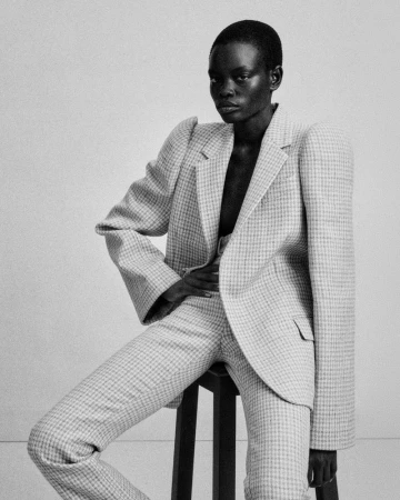 Model Athiec Geng seated on a stool wearing an exaggerated shoulder houndstooth suit in black and white for Acne Paper.