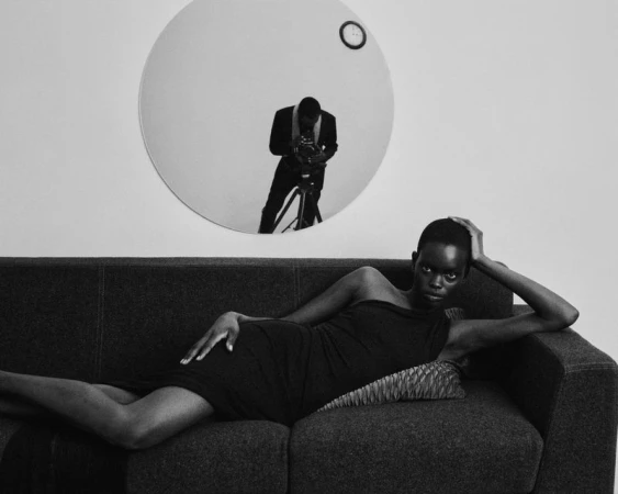 Black and white photo of model Athiec Geng reclining on a dark couch below a round mirror reflecting photographer Malick Bodian.
