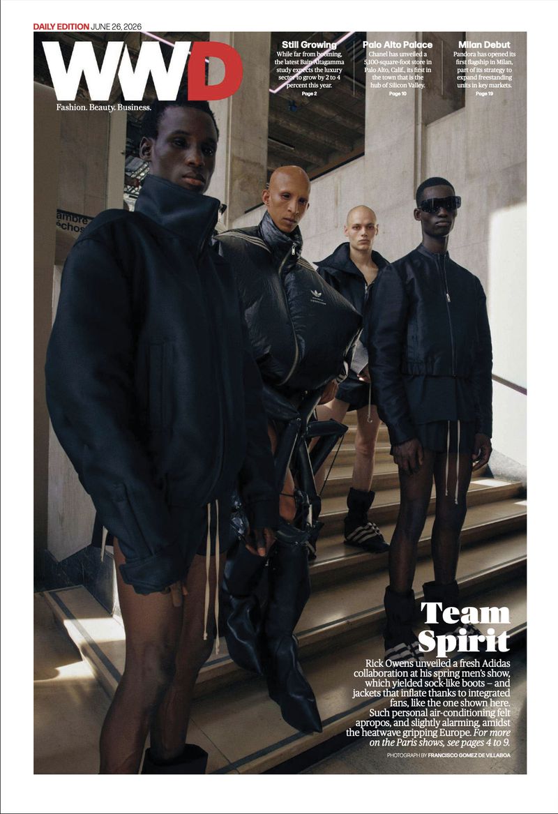 Four male models wearing black sculpted jackets, shorts, and boots standing on concrete stairs for WWD Rick Owens coverage.