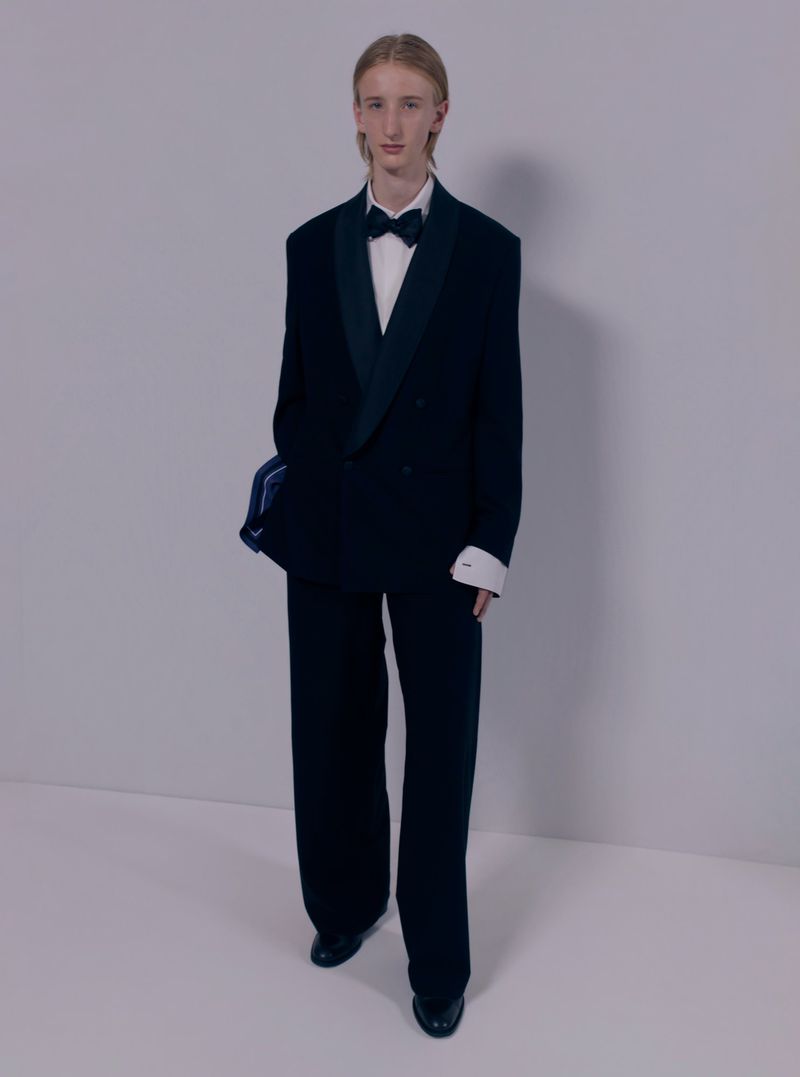 Male model wearing a double-breasted black tuxedo with a black bow tie and white dress shirt against a neutral studio backdrop.