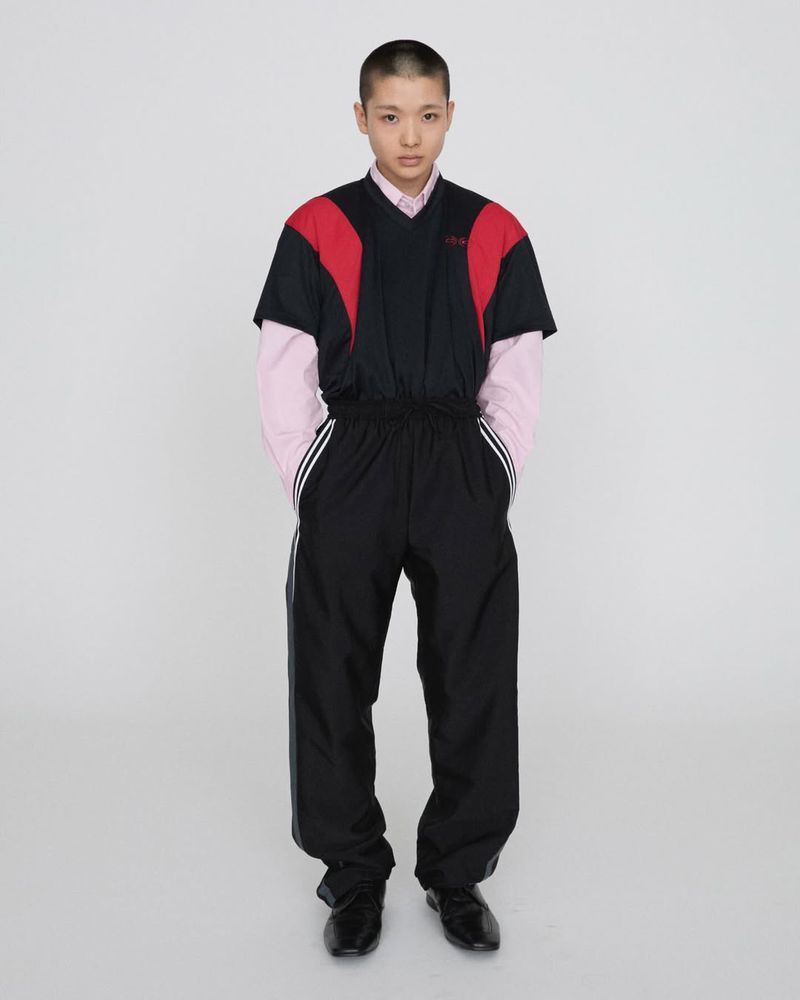 Full-length shot of a model posing in a black and red tracksuit against a white background in a studio environment. Fashion.