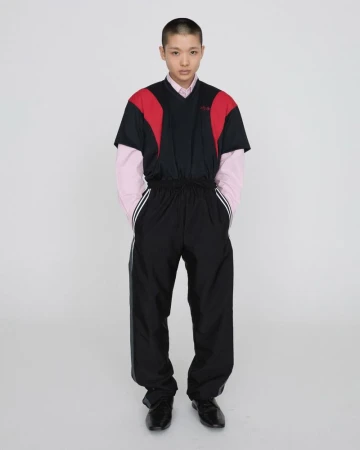 Full-length shot of a model posing in a black and red tracksuit against a white background in a studio environment. Fashion.
