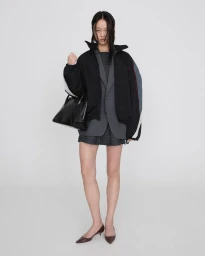 Model in grey plaid blazer and black jacket holding handbag against white background