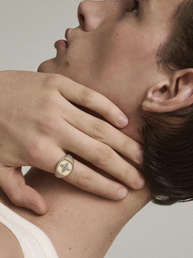 Close-up of a man with his hand on his neck, wearing an engraved gold and enamel signet ring on his pinky finger.
