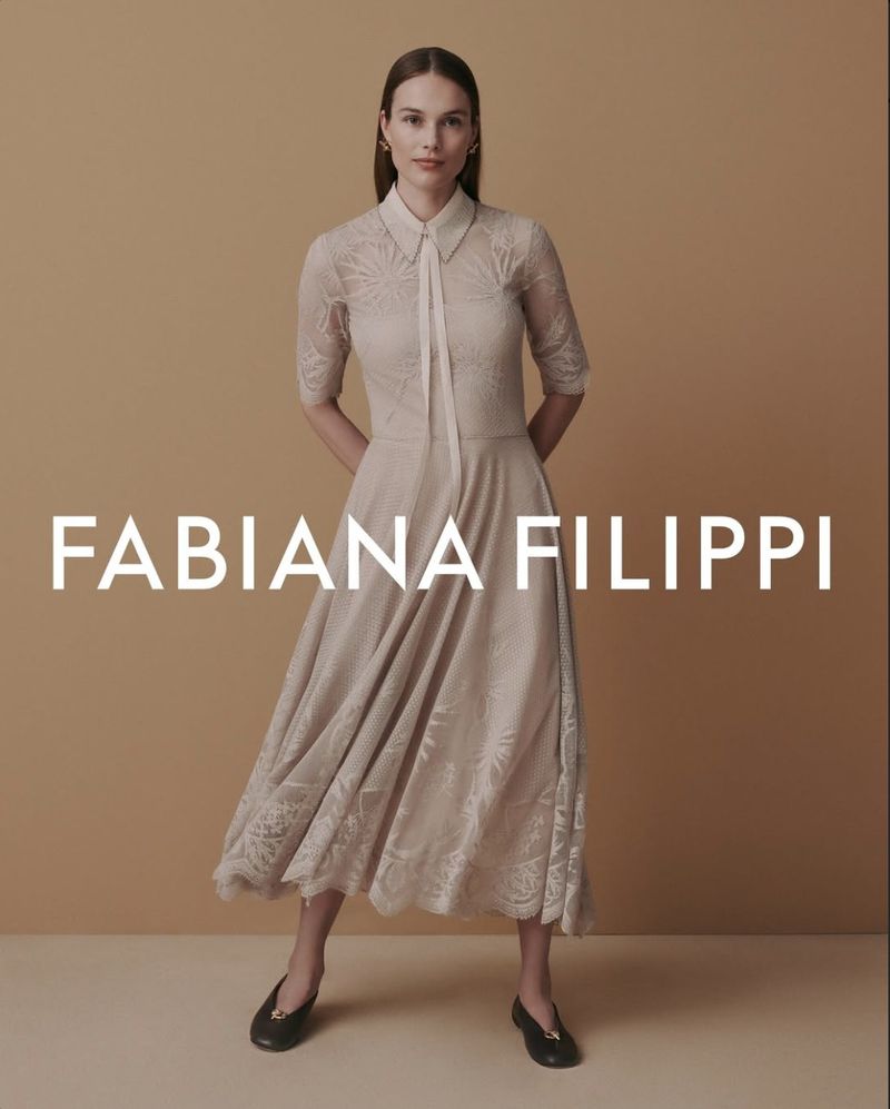 Model Rozanne Verduin in a collared beige lace midi dress and black ballet flats against a warm tan studio backdrop.