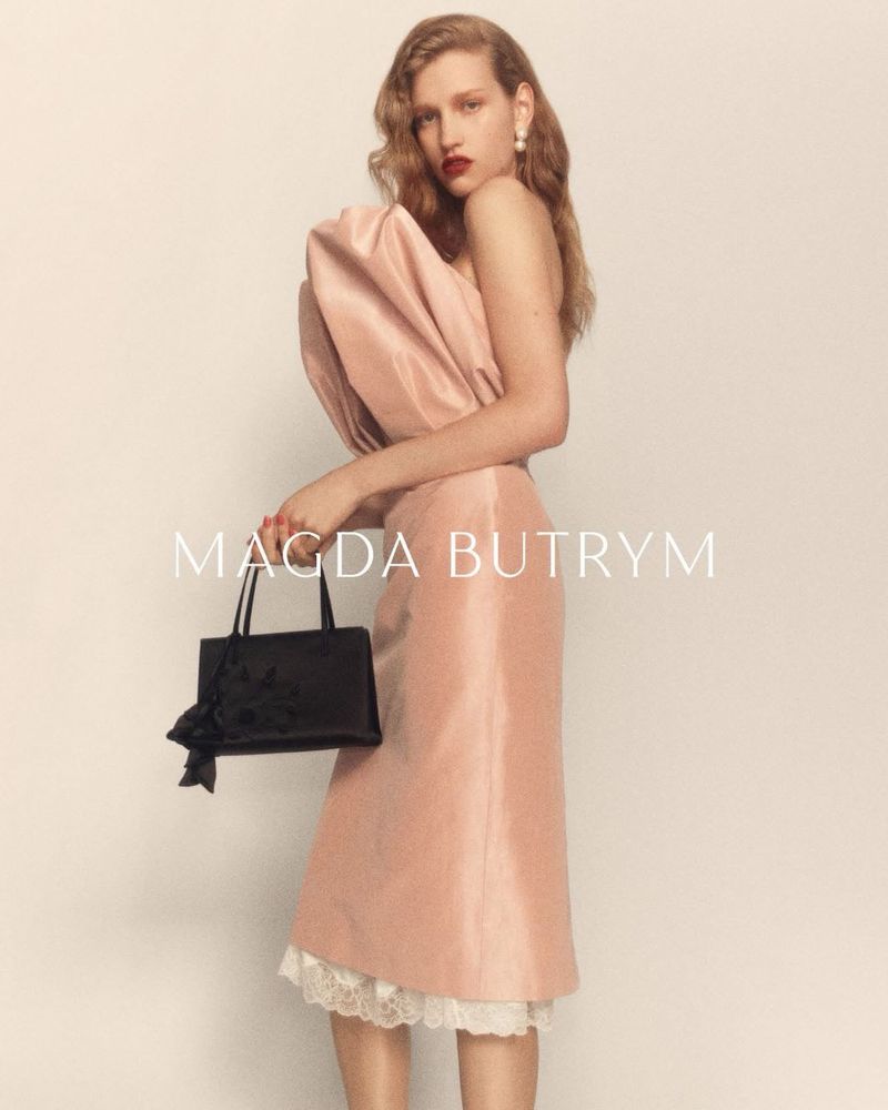 Apolline Rocco Fohrer in a sculptural blush strapless dress with lace trim, holding a small black handbag against a studio backdrop.