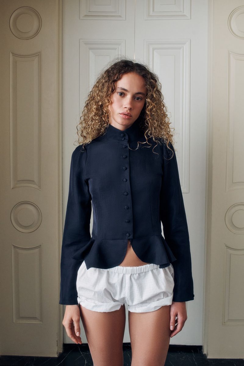 Model in a black button-down peplum top and white bloomer shorts posing before panelled white interior doors.