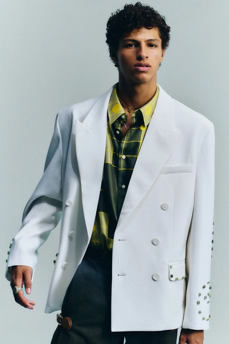 Model Adam Gerphagnon posing in an oversized white double-breasted blazer and green patterned shirt against a grey studio backdrop.