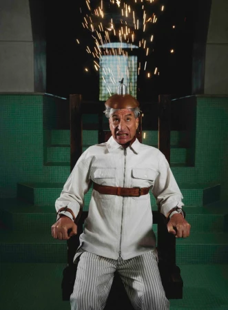 Maurizio Cattelan strapped into an electric chair with sparks flying from his helmet for Hube Magazine.