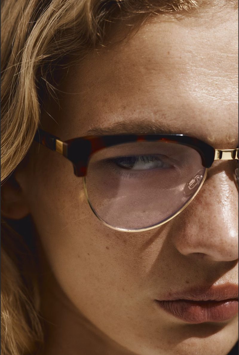 Close-up portrait of a blond adult female with fair skin and freckles wearing clear eyeglasses with a tortoiseshell and gold frame.