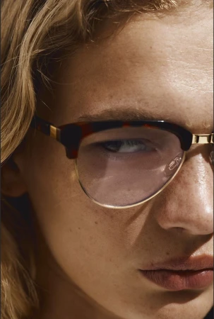 Close-up portrait of a blond adult female with fair skin and freckles wearing clear eyeglasses with a tortoiseshell and gold frame.