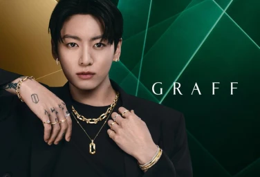 Jung Kook wearing gold chains and diamond rings from the Laurence Graff Signature collection against an emerald green background.