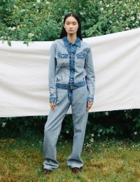 Model standing outdoors wearing a contrasting two-tone denim jacket and matching jeans in front of a white cloth backdrop