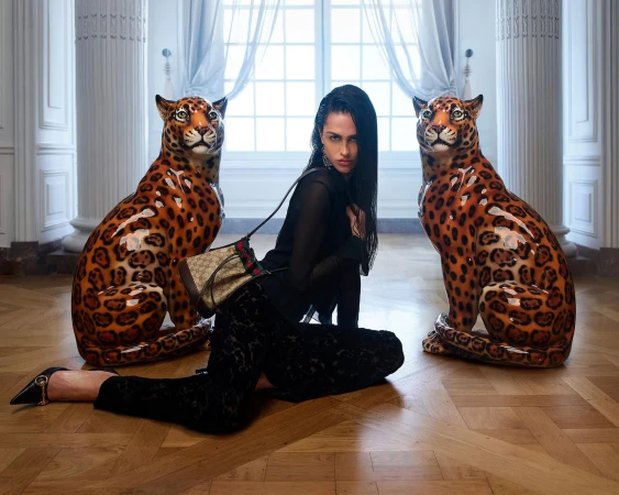Model Amelia Gray posing between two ceramic leopard statues on a parquet floor with a Gucci monogram bucket bag.
