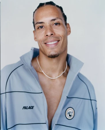 Portrait of Virgil van Dijk wearing a light blue zip jacket and a beaded necklace against a white background