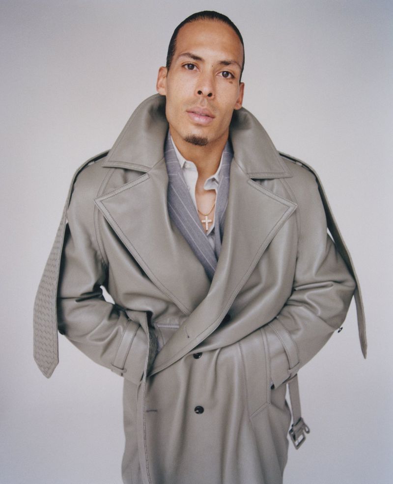 Virgil van Dijk wearing an oversized grey leather trench coat and gold cross necklace in a studio portrait.