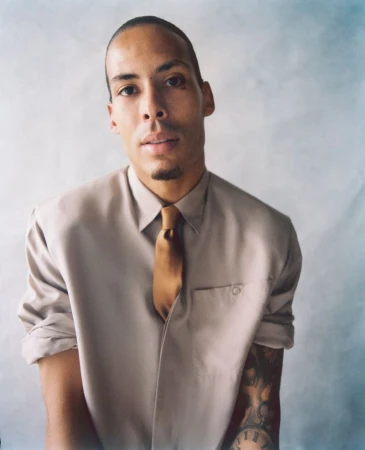 Virgil van Dijk wearing a beige collared shirt and golden brown tie against a textured studio backdrop.