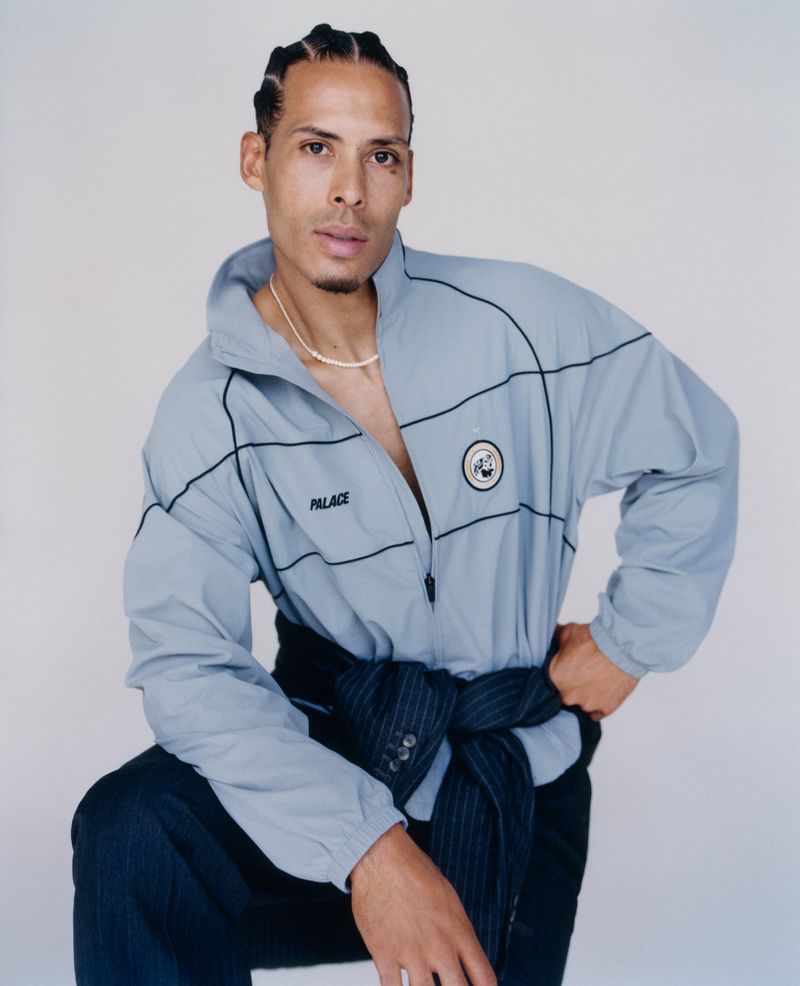 Virgil van Dijk wearing a light blue zip-up track jacket with dark pants against a plain white studio backdrop.