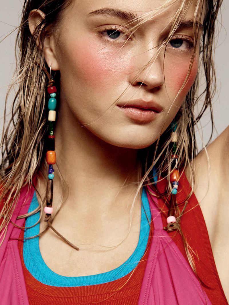Ciara Hammett wearing long beaded earrings, layered pink, red, and blue tank tops against a grey studio backdrop.