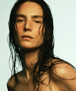 Close-up portrait of model Mijo Mihaljcic with wet dark hair and bare shoulders against a pale backdrop.