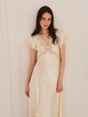 Elegant woman poses in a pale yellow vintage gown with lace details against a neutral background, showcasing fashion and style.