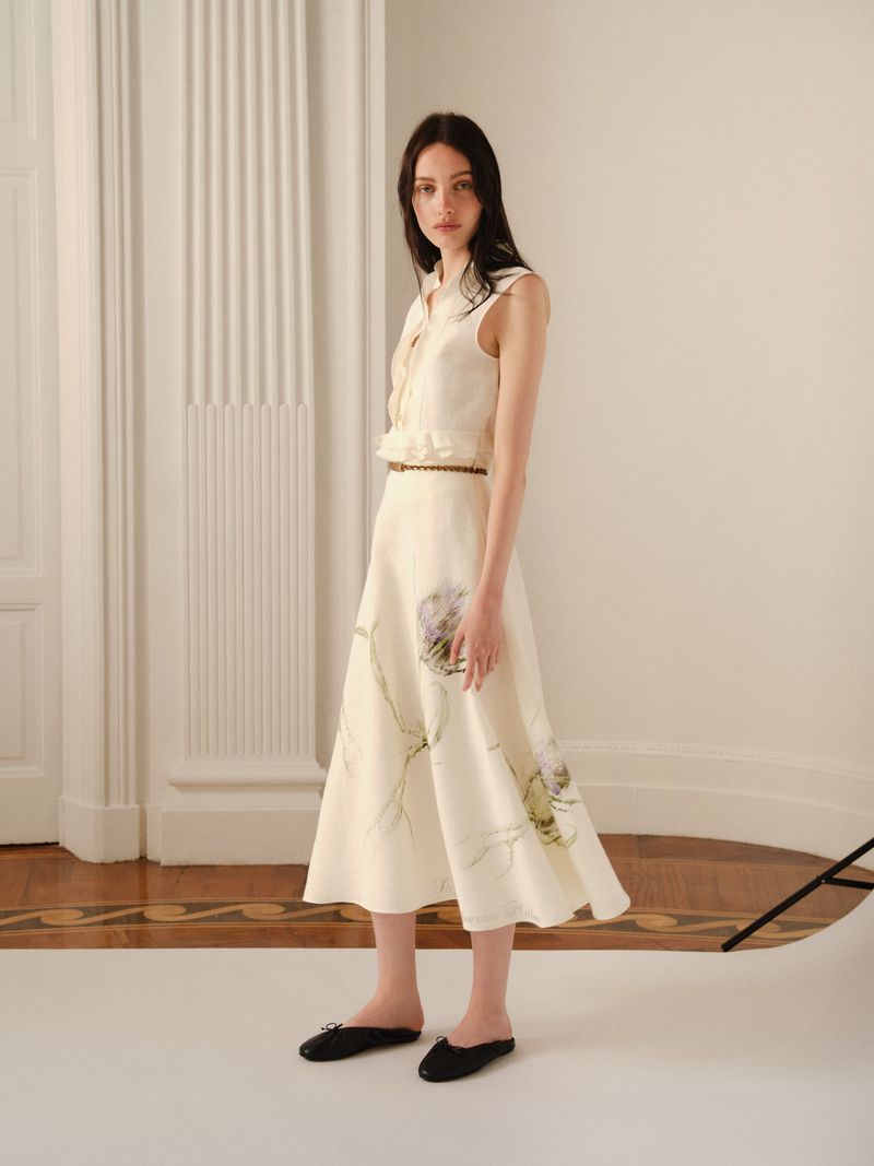 Elegant woman in a sleeveless top and midi skirt with a floral pattern poses in a brightly lit indoor space with hardwood floors.